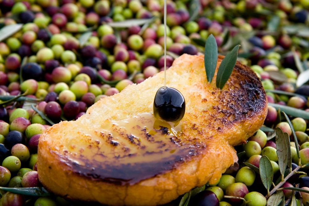 sobre un montón de aceitunas hay una tostada a la que le echan aceite